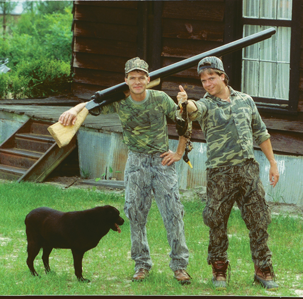 tk and mike stand with an comically large shotgun and a duck