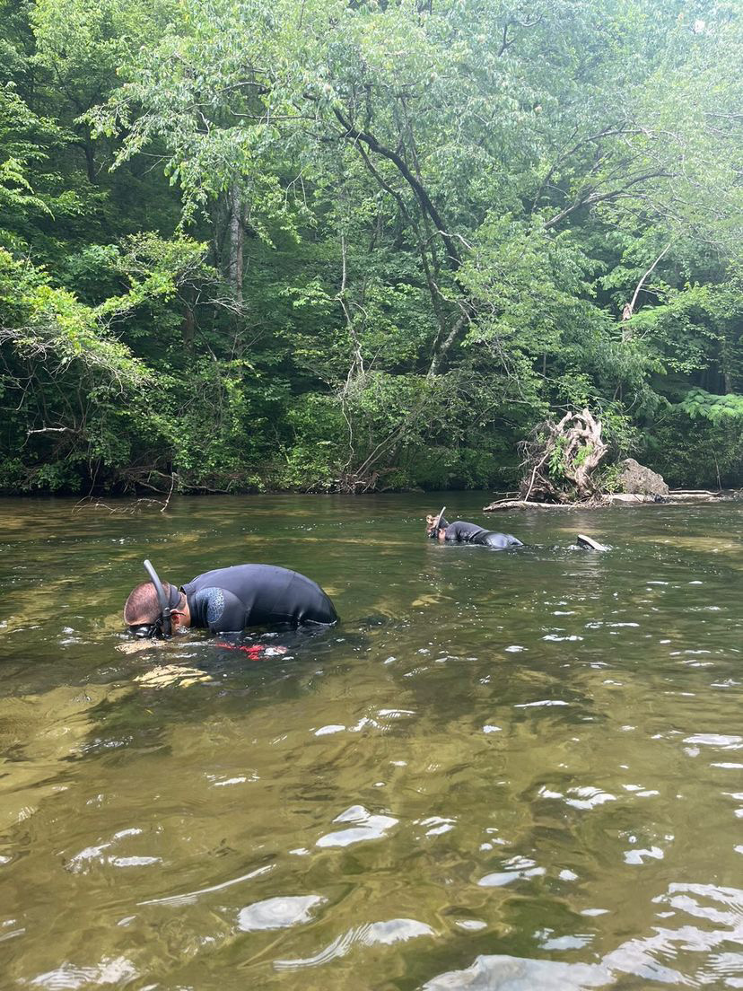 two people snorkel in wetsuits in a shallow stream
