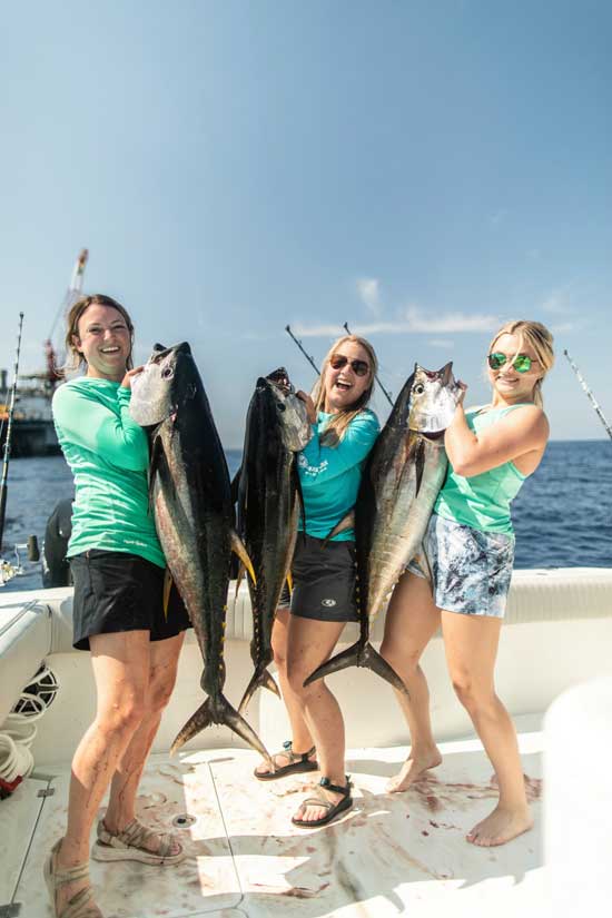 three girls each holding up a tuna