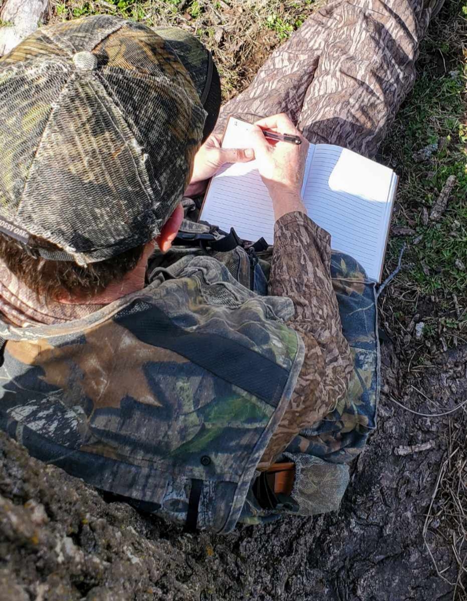 man writes in journal in the woods