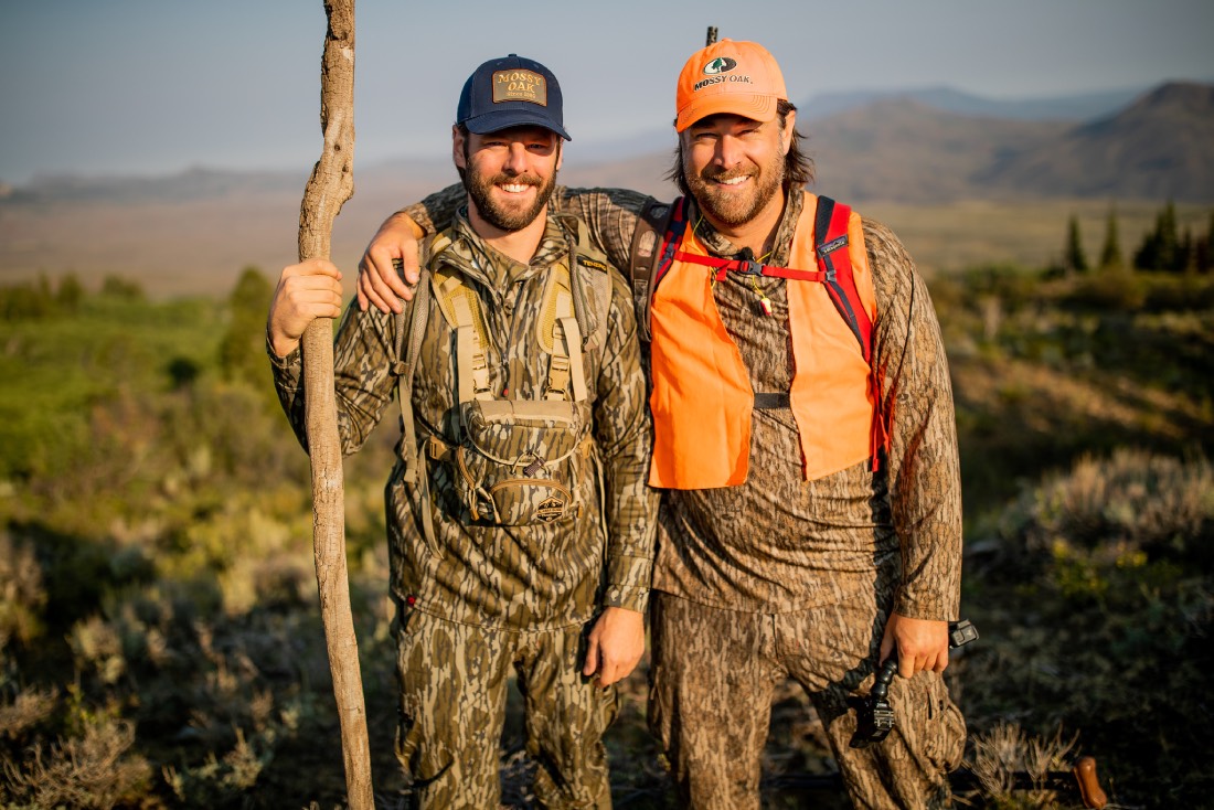 two men stand in bottomland camo amidst elk country