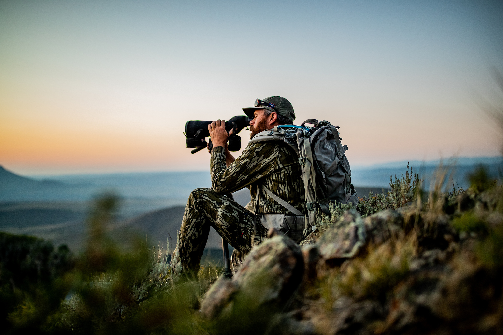 man sits on a mountain with a spotting scope