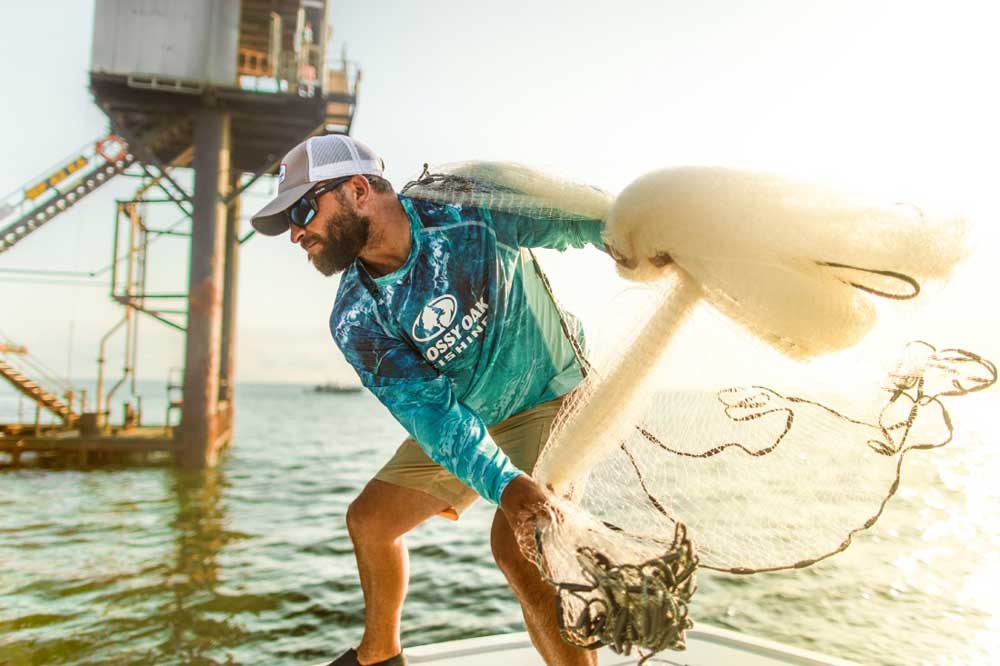 man slinging a net for baitfish near an oil rig