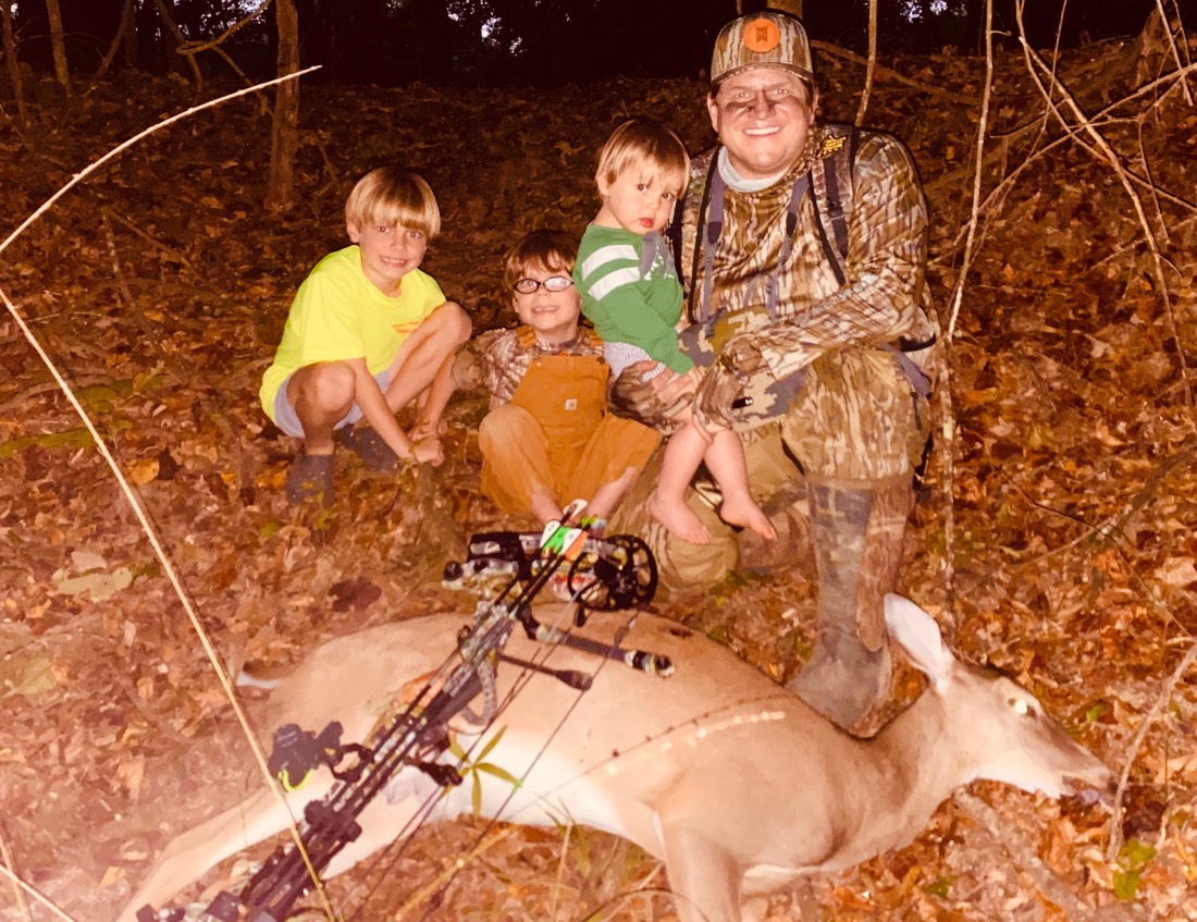 Taylor sledge posts in front of a deer with his three young sons